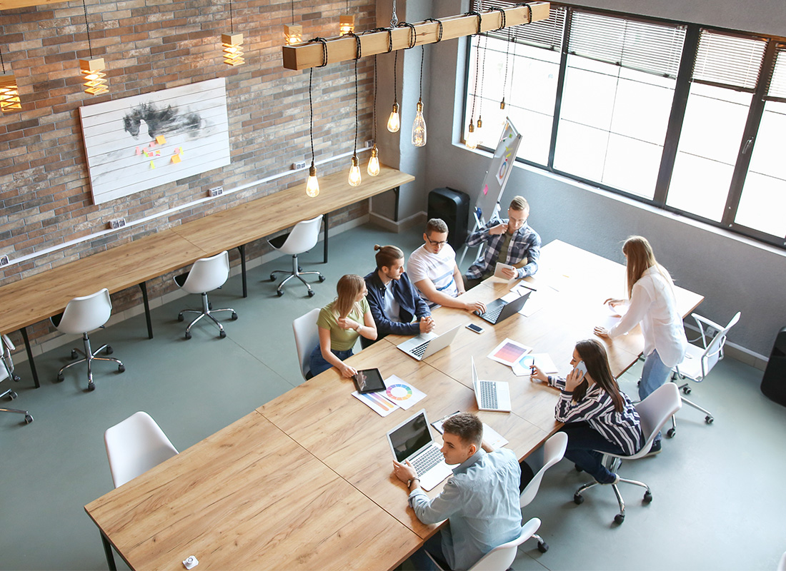 Sauk Centre, MN - Modern Office Space From Above With Business Team Working Collaboratively at Rectangular Wooden Table With Laptops
